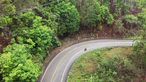 Aerial-shot-of-bike-riding-in-the-curvy-street-in-between-the-dense-forest