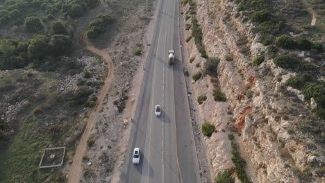 Aerial-bird's-eye-shot-over-a-highway-road-through-spruce-forest-trees-on-the-hilly-terrain-in-Israel,-Katzir-at-daytime