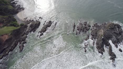 Waves-With-Foam-Splashing-On-Rocky-Shore-At-Broken-Head,-New-South-Wales,-Australia---aerial-top-down