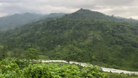 Filmische-Malerische-Landschaft-Von-Bhutan,-Wie-Sie-Von-Indien-Aus-Gesehen-Wird,-Mit-Einem-Fluss,-Der-Durch-Die-Grüne-Bergkette-Fließt