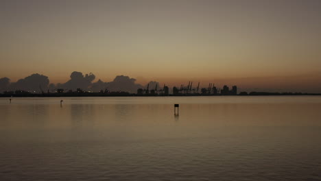 Descending-aerial-view-shipping-port-cranes-silhouette-markets-on-Miami-coastline-during-sunset