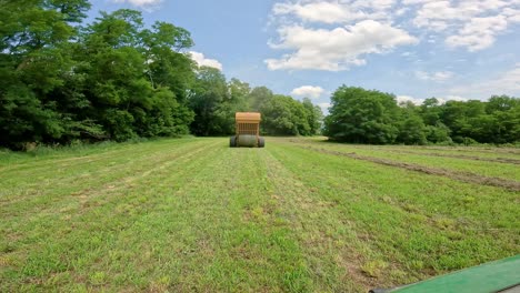 View-from-back-of-yellow-hay-baler-ejecting-a-finished-large-round-bale-of-hay-in-an-alfalfa-field
