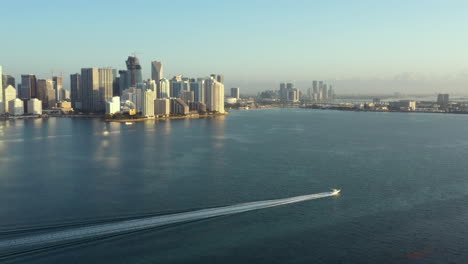 Aerial-rising-view-speedboat-cruising-Miami-waterfront-under-city-skyscraper-skyline