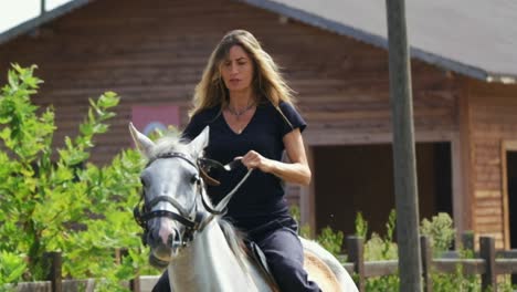 Adult-woman-rides-white-horse-in-horse-farm