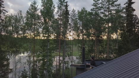 AERIAL-shot-of-woman-enjoying-view-at-Nordic-summer-cabin,-scandinavian-quality-of-life-concept
