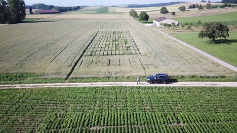 Drone-view-of-a-stationary-xc90-SUV-Volvo-car-on-a-bumpy-road-in-between-agriculture-Fields-in-the-Swiss-countryside,-Vaud