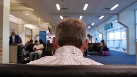 4k-Businessman-waiting-for-flight-at-airport-or-bus-stop-behind-head-in-crowded-lobby-or-terminal