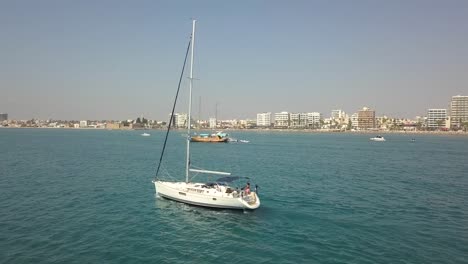 Tracking-Shot-Of-Sailing-Boat-Cruising-In-Blue-Sea-In-Front-Of-Larnaca-City-Bay,-Cyprus
