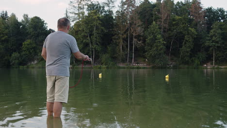 A-man-standing-in-a-lake,-throwing-a-rope-with-a-magnet-into-the-water