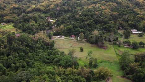 Aerial-drone-forward-moving-shot-over-cottages-surrounded-by-lush-green-vegetation-on-the-outskirts-of-Tham-Pla-Pha-Suea-National-Park-at-daytime