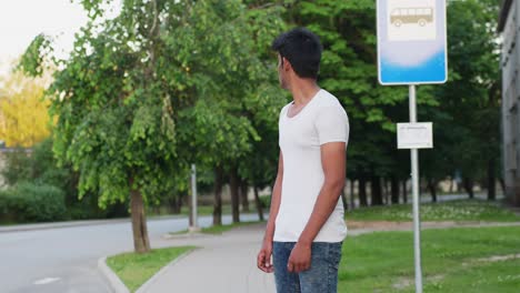 Young-asian-male-in-white-shirt-waiting-at-the-bus-stop