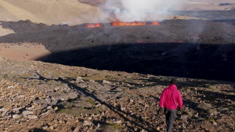 Guy-walking-on-rugged-hill-overlooking-natural-phenomenon-fissure-volcano-eruption-in-Iceland,-2022