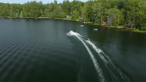 Aerial-drone-following-shot-of-a-water-skier-being-pulled-by-a-speedboat-on-sunset-lake,-New-Hampshire,-USA