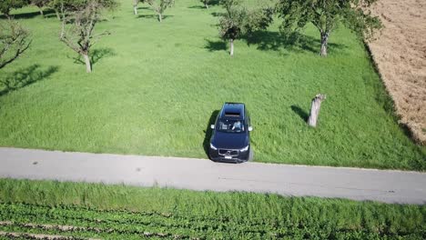 a-xc90-volvo-suv-car-turns-180-degrees-on-the-bumpy-swiss-country-road-encroaching-on-the-field-in-order-to-go-back-in-the-opposite-direction,-aerial-drone-shot