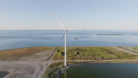 An-aerial-view-In-a-calm-sunny-evening,-wind-turbine-blades-slowly-rotate-and-you-can-see-the-Baltic-Sea-in-the-background