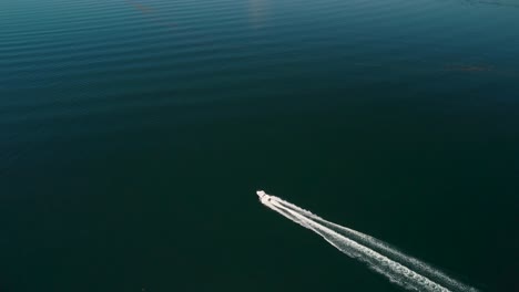 Aufsteigende-Drohnenaufnahme-Eines-Bootes,-Das-über-Die-Oberfläche-Eines-Sees-Rast