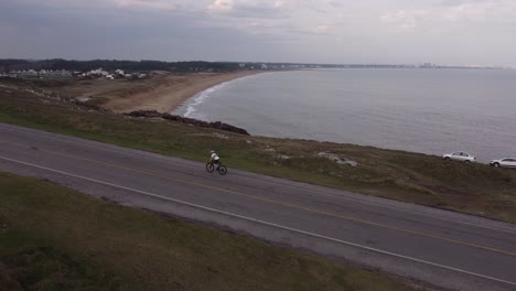 Aerial-view-orbiting-cyclist-on-Punta-Ballena-road,-Uruguay