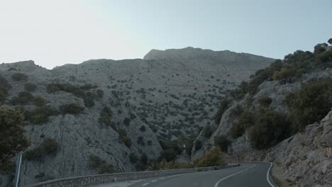 wide-shot-of-curve-road-over-Tramuntana-mountains,-Mallorca-during-sun-rays-on-sunny-day