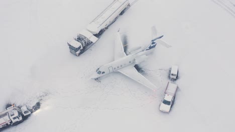 Embraer-business-jet-on-snowy-tarmac-with-support-vehicles,-aerial