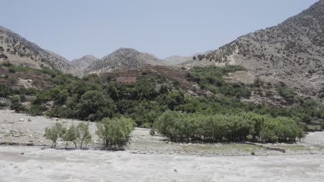 Muddy-water-stream-flowing-through-Panshir-valley-in-Afghanistan,-tilt-up-view