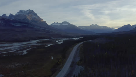 Rocky-Mountain-peaks-rise-above-road-through-river-valley,-Alberta,-Canada