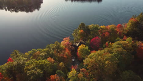 Drone-coming-over-the-Autumn-fall-colors-of-the-woods-to-the-lake-with-cottage-and-boats,-muskoka,-canada