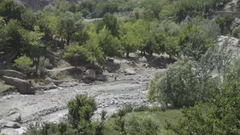 Dry-river-surrounded-by-green-foliage-in-Panshir-valley,-with-child-playing