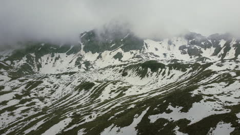 Día-De-Invierno-Nublado-En-Zernez-Suiza-Con-Nubes-Rodando-Sobre-Picos-Montañosos-Cubiertos-De-Nieve,-Zoom-De-Muñeca-Aérea