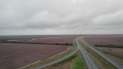AERIAL---Completely-empty-highway-next-to-fields,-cloudy-day,-Reynosa,-Tamaulipas,-Mexico