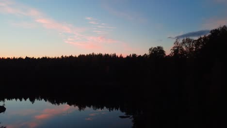 Aerial-view-through-forest-and-over-a-reflecting-lake,-fall-sunset-in-Finland---rising,-drone-shot
