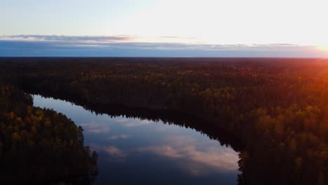Aerial-view-over-a-reflecting-forest-lake,-autumn-sunset-in-Finland---circling,-drone-shot