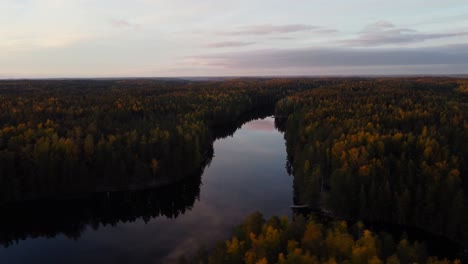 Aerial-view-around-a-mirroring-forest-lake-on-a-sunny-fall-evening-in-Espoo,-Finland---circling,-drone-shot