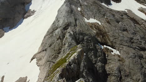 wide-aerial-of-sharp-mountain-peak-covered-in-snow-during-summer-day