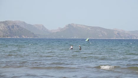 One-Person-gets-kiteboarding-lessons-in-cear-blue-water-at-Mallorca-Balearic-Islands-surrounded-by-mountain-and-a-windfoil-surfer