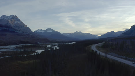 Car-drives-lonely-road-through-river-valley,-Nordegg,-Alberta