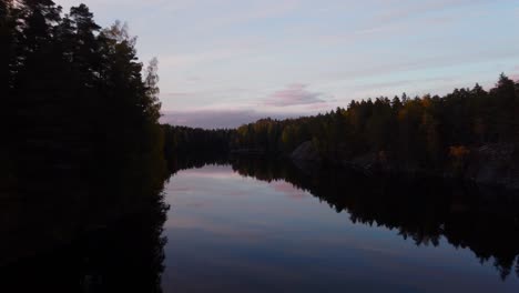 Aerial-view-over-a-reflecting-lake,-autumn-dusk-in-Finland---low,-drone-shot