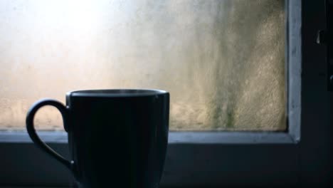 Handheld-detail-shot-of-a-cup-with-steaming-hot-tea-on-a-windowsill