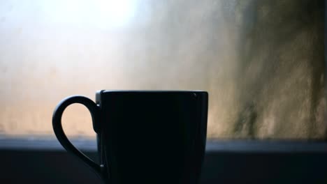 Close-up-of-a-cup-with-hot-drink-standing-on-a-windowsill