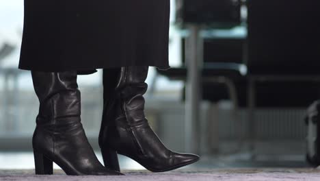 a-nervous-businesswoman-in-a-dress-wears-shiny-black-boots-she-walks-into-the-picture,-zoom-in
