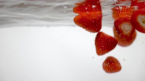 Red-strawberries-dropping-into-fresh-water,-floating-on-surface
