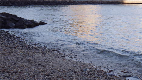 Schattiger-Kiesstrand-Mit-Ozeanwellenbuffet-Und-Reflexion-Der-Brooklyn-Bridge,-Handgerät