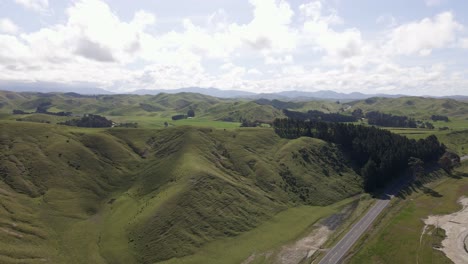 Lush-hills-and-meadows-in-sunny-New-Zealand-with-an-empty-countryside-highway-in-foreground
