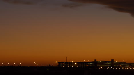 Pan-right-shot-of-Barcelona-Airport-lit-up-at-sunset-revealing-plane-landing