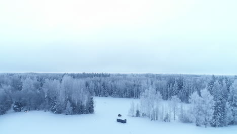Wooden-cabin-and-Sauna-in-the-middle-of-snow-covered-winter-forest,-Aerial-shot