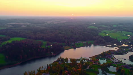 Aerial-drone-shot-over-majestic-autumn-landscape-over-Baltezers-estate-with-beautiful-sunrise-sky-reflection-on-lake-river-surrounded-by-dense-vegetation-in-Latvia