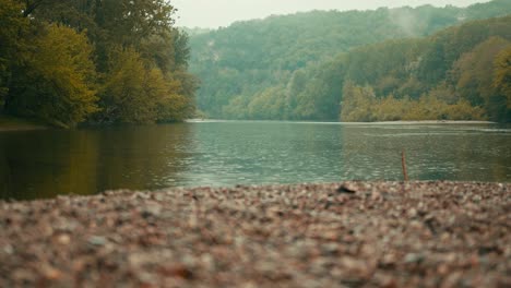 River-in-autumn-with-pebbles-traveling-sideways,-a-little-drume-in-the-background-on-the-hills