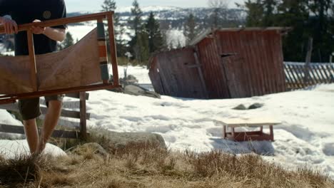 Man-setting-up-and-sits-down-in-a-folding-char-in-the-sun-in-spring-in-norway-with-some-snow-left-on-the-ground