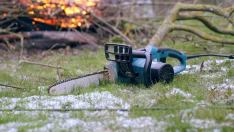 Cutting-wood-for-winter-concept,-chainsaw-outside-snow-with-fire-on-background