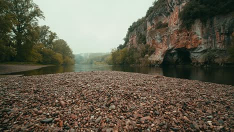 at-the-edge-of-a-river-in-autumn-the-Dordogne,-French-river,-tracking-shot-with-cliffs