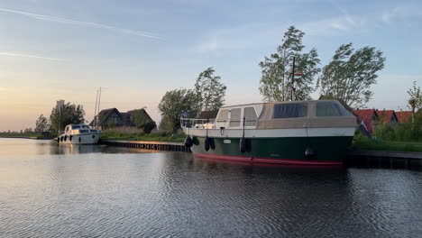 Kreuzfahrt-über-Den-Fluss-Vorbei-An-Booten-Am-Flussufer-In-Der-Nähe-Des-Luxusferienparks-In-Ossenzijl,-Niederlande-Bei-Sonnenuntergang